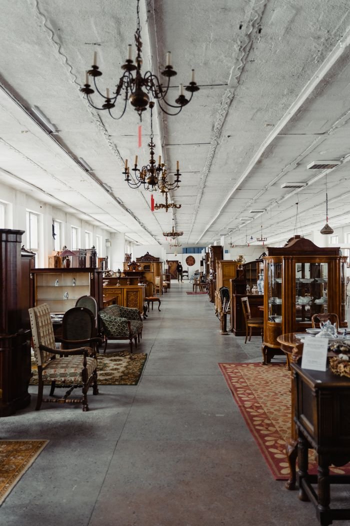 A long aisle in a vintage furniture store showcasing antique wooden pieces and chandeliers.